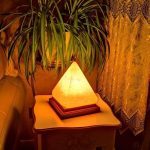 Warm beleuchtete Himalaya-Salzlampe in Pyramidenform auf Nachttisch neben Zimmerpflanze, schafft eine gemütliche Atmosphäre.