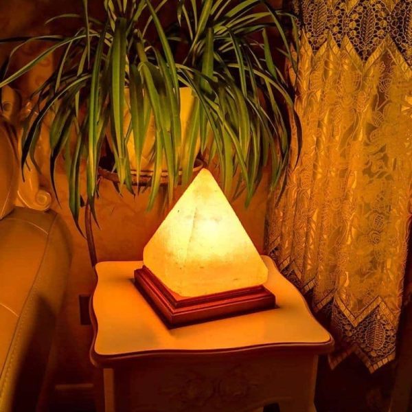 Warm beleuchtete Himalaya-Salzlampe in Pyramidenform auf Nachttisch neben Zimmerpflanze, schafft eine gemütliche Atmosphäre.