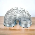 Metallischer wissenschaftlicher Gegenstand in einer spiralförmigen Form, ideal für Dekoration und Gadgets, auf Holzoberfläche präsentiert.
