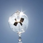 Sphärisches Pendel mit Solarzellen, das die Energieübertragung durch Licht zeigt, vor hellem Himmel.