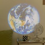 Projektion der Erde an die Wand, mit Globus und Tasse auf einem Nachttisch, ideal für wissenschaftliche Dekorationen und Lernräume.