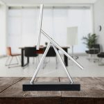 Ein modernes wissenschaftliches Dekorationsstück aus Metall, das an ein geometrisches Experiment erinnert, auf einem Holztablett präsentiert.