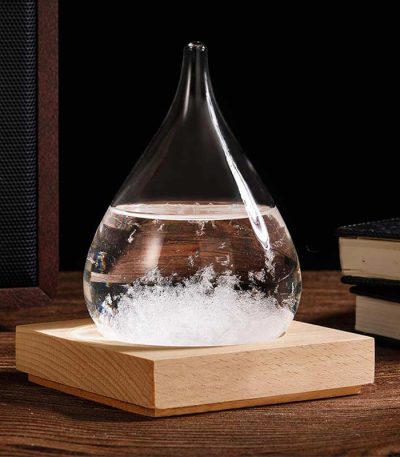 Ein Glas mit einer chemischen Reaktion, die Blasen und Schaum erzeugt, steht auf einem Holzsockel. Das Bild zeigt ein wissenschaftliches Experiment oder Dekorationsobjekt.