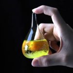 Hand hält ein Reagenzglas mit gelber Flüssigkeit und Bläschen, wissenschaftliches Experiment, Nahaufnahme.