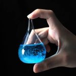 Hand hält ein Reagenzglas mit leuchtend blauer Flüssigkeit gegen schwarzen Hintergrund, Wissenschafts- und Laborequipment.