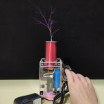 Hochspannungs-Generator erzeugt elektrische Funkenentladungen, sichtbar durch die bläulichen Blitze an der Spitze des roten Zylinders, ideal für wissenschaftliche Demonstrationen.