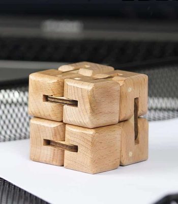 Holz-Puzzle-Objekt mit verschlungenen Teilen, das auf einer weißen Oberfläche liegt, vor einem dunklen Hintergrund.