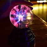 Eine Blitzkugel mit leuchtendem Plasma-Effekt, die von einer Hand gehalten wird, zeigt beeindruckende elektrische Entladungen in einem dunklen Raum.