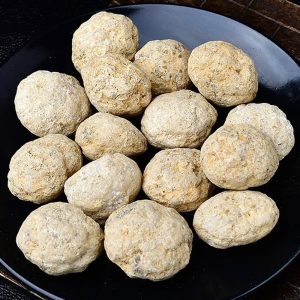 Nahaufnahme von kleinen, runden Steinbällchen auf einem schwarzen Teller, ideal für wissenschaftliche Demonstrationen und Experimente.