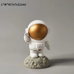 Kleiner Astronauten-Statue mit goldfarbenem Helm, stehend auf einem Mond-ähnlichen Felsen, ideal für Wissenschafts- und Dekorationszwecke.