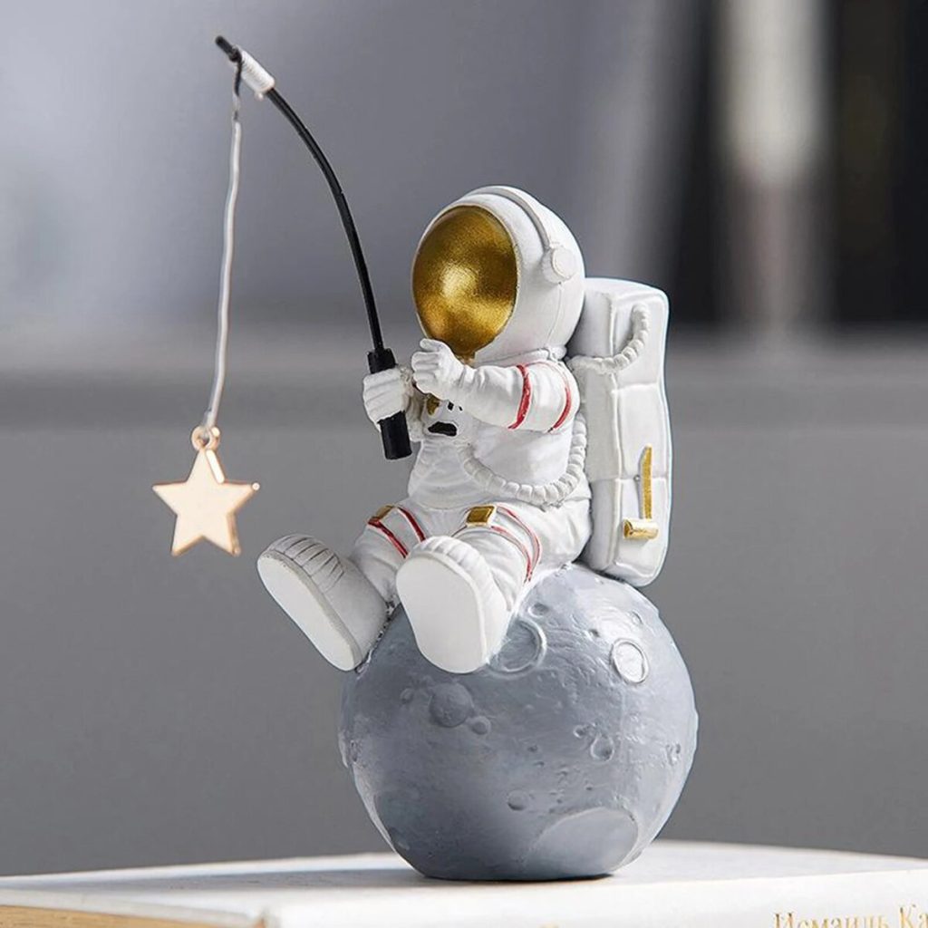 Niedliches Raumfahrer-Design mit Astronautenfigur, die auf einem Mond sitzt und einen Sternanhänger hält, ideal für Wissenschafts- und Dekorationsliebhaber.
