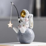 Niedliches Raumfahrer-Design mit Astronautenfigur, die auf einem Mond sitzt und einen Sternanhänger hält, ideal für Wissenschafts- und Dekorationsliebhaber.