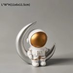 Kleine Astronautenfigur mit goldenem Helm, die auf einer silbernen Mondhalterung steht, ideal für wissenschaftliche Dekorationen und Sammlerstücke.