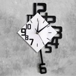Zeitmesser mit quadratischem Zifferblatt und schwarzen Zahlen, kombiniert mit einem schwarzen Pendel, an einer grauen Betonwand.