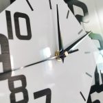 Nahaufnahme einer modernen Wanduhr mit schwarzem Zifferblatt, weißen Zahlen und silbernem Rahmen, zeigt die Zeit bei 2:00 Uhr.