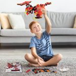 Junge spielt mit einem roten und schwarzen LEGO Feuerdrachen, der fliegend in der Luft schwebt, im Wohnzimmer.