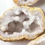 Nahaufnahme eines mineralischen Geoden-Kristalls mit weißen, glitzernden Kristallen im Inneren, umgeben von einer rauen, gelblichen Außenhülle.