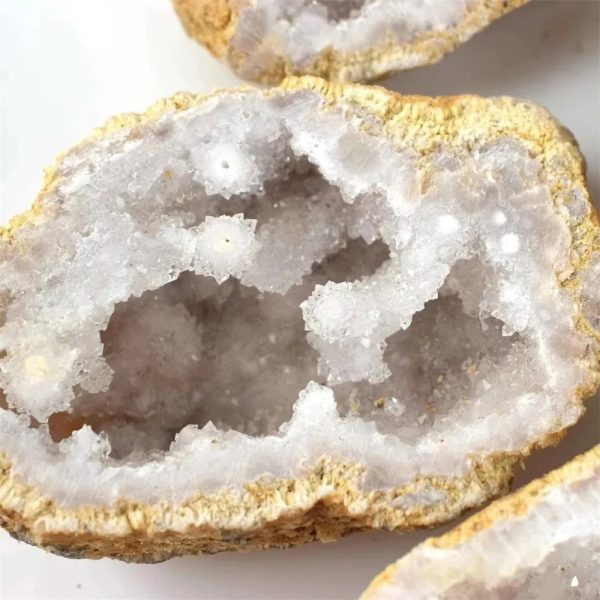 Nahaufnahme eines mineralischen Geoden-Kristalls mit weißen, glitzernden Kristallen im Inneren, umgeben von einer rauen, gelblichen Außenhülle.