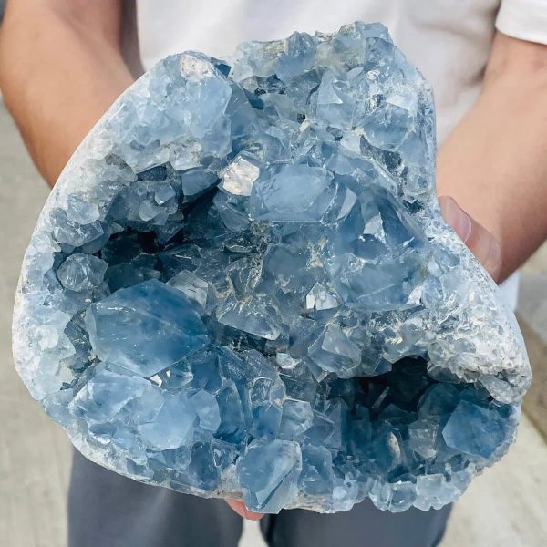 Großes, bläuliches Kristallgestein mit vielen Facetten, gehalten von einer Person, zeigt die natürliche Schönheit und Transparenz des Minerals.