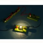 Wissenschaftliches Experiment mit Hochspannung, das einen Lichtbogen zwischen zwei Elektroden zeigt, auf einer grünen Basis mit Stromquelle.
