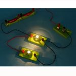 Elektrischer Schaltkreis mit leuchtenden Glühbirnen, verbunden durch rote und schwarze Drähte auf blauer Oberfläche.