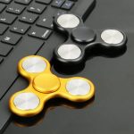 Zwei Fidget-Spinner, einer in Gold und einer in Schwarz, liegen auf einer Tastatur und einem Tisch, ideal für Stressabbau und Konzentrationsförderung.