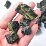 Hand hält mehrere grüne und schwarze mineralische Steine, ideal für wissenschaftliche Dekorationen und Sammlungen.