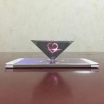 Holografischer Projektor mit Herz-Design, der auf einem Smartphone liegt, erzeugt eine schwebende Herzform in der Luft. Perfekt für romantische Dekorationen und wissenschaftliche Experimente.