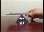 Ein Smartphone, das auf einer transparenten Kristallbasis steht, die Licht reflektiert, mit einer Hand, die es vorsichtig hält, auf einem dunklen Tisch.
