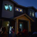 Haus mit leuchtenden Geister- und Augen-Dekorationen, Halloween-Atmosphäre bei Nacht, Kinder schauen fasziniert.