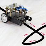 Kleiner Wissenschaftsroboter auf weißem Hintergrund, der Linien auf dem Boden folgt, mit sichtbaren Sensoren und elektronischen Komponenten.