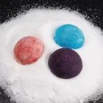 Bunte mineralische Pigmente in Pulverform auf weißem Sand, ideal für wissenschaftliche Experimente und kreative Dekorationen.