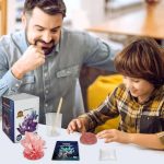 Ein Vater und sein Sohn führen ein wissenschaftliches Kristall-Experiment mit einem Kristall-Set, einem Smartphone und weiteren Materialien auf einem Tisch durch.