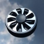 Runder Gegenstand mit schwarzen Propellerblättern auf Wasser, reflektiert den Himmel und Wolken.