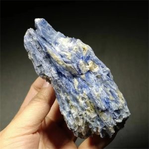 Himmelsblauer Mineralstein, handgehalten, mit kristalliner Struktur und bläulichen Tönen, auf dunklem Hintergrund.