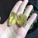 Nahaufnahme von goldgelben Kristallen, die auf einer Hand liegen, mit weiteren Kristallen im Hintergrund. Perfekt für wissenschaftliche Dekorationen und Sammlerstücke.