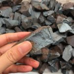 Hand hält einen großen, rauen Steinbrocken vor einer Vielzahl ähnlicher Steine im Hintergrund. Perfekt für wissenschaftliche oder dekorative Zwecke.