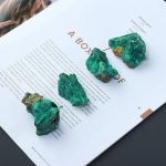 Drei grüne Mineralproben auf einer Zeitschrift, ideal für wissenschaftliche Dekorationen und Sammlungen. Perfekt für Liebhaber von Naturwissenschaften und Mineralien.