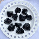 Zehn schwarze Obsidian-Kristalle auf einer weißen, dekorativen Platte, ideal für wissenschaftliche Dekorationen oder Kristallsammlungen.