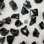 Natürliche schwarze Obsidian Kristalle, unregelmäßig geformt, auf hellem Hintergrund mit Münze für Größenvergleich. Perfekt für Dekoration und wissenschaftliche Sammlungen.