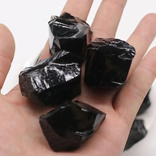 Nahaufnahme von schwarzen Obsidian-Steinen, die auf einer Hand liegen, mit glänzender, glasartiger Oberfläche. Perfekt für wissenschaftliche Dekorationen und Mineralien-Sammlungen.