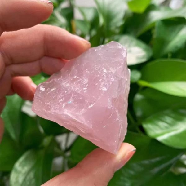 Rohes Rosenquarz-Fragment, handgehalten vor grünen Blättern, natürliche Mineralien, Schmuckstein, Heilstein, Dekoration, Edelstein, Kristall, Naturprodukt, spirituelle Energie.