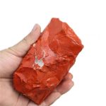 Hand hält einen roten, unregelmäßig geformten Mineralstein mit glänzender Oberfläche, ideal für wissenschaftliche Dekorationen oder Sammlerstücke.