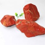 Drei Stücke natürlicher roter Felsen mit goldenen Adern, auf weißem Hintergrund angeordnet, illustrieren ein dekoratives oder pädagogisches wissenschaftliches Objekt.