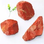 Drei rote Steine mit natürlicher Textur, ideal für wissenschaftliche Modelle oder dekorative Zwecke, auf weißem Hintergrund mit kleiner grüner Pflanze.