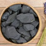 Natürliche schwarze Schiefersteine in einem runden Holzbehälter, ideal für wissenschaftliche Dekorationen und kreative Projekte.