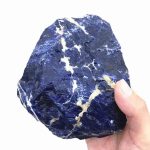 Hand hält einen großen, rohen Sodalith-Stein mit blauer und weißen Adern, ideal für wissenschaftliche Dekorationen und Lernzwecke.