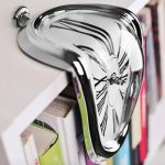 Moderne Schmelz-Uhr aus glänzendem Metall mit verzerrtem Zifferblatt, die an eine geschmolzene Uhr erinnert, ideal als wissenschaftliches Dekorationsstück.