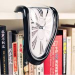Ein surrealistischer Wecker, der wie geschmolzen wirkt, hängt an einem Bücherregal. Das Design erinnert an Salvador Dalís berühmte Uhren, die die Zeit in einer träumerischen, verzerrten Form darstelle.