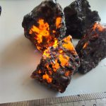 Nahaufnahme von einem Feuerstein mit leuchtenden orangefarbenen Lava-ähnlichen Strukturen, die im Inneren glühen, auf weißem Hintergrund.